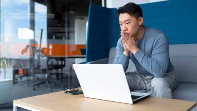 A Chinese investor sits in front of his laptop looking pensive and concerned about pandemic lockdowns which may impact ASX 200 iron ore share prices