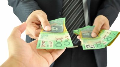 Nickel Mines executive wearing a black suit hands back $100 dollar bills to an ASX shareholders as the share purchase plan is cancelled
