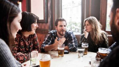 A group of friends sit at a table in a pub drinking beer and socialising