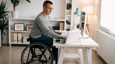 Man in a wheelchair at a desk, checking his computer.