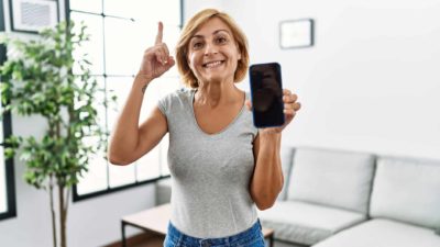 A woman shows her phone screen and points up.